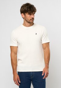 Kortærmet, cremefarvet t-shirt med tekstureret stof, rund udskæring og et lille navy-logo på brystet.