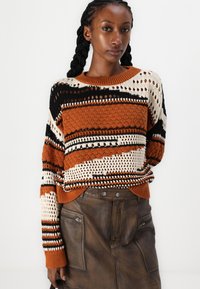 Maglione lavorato a maglia con strisce arancioni, nere e crema, caratterizzato da una texture a punto aperto e un collo rotondo, abbinato a una gonna di pelle marrone.