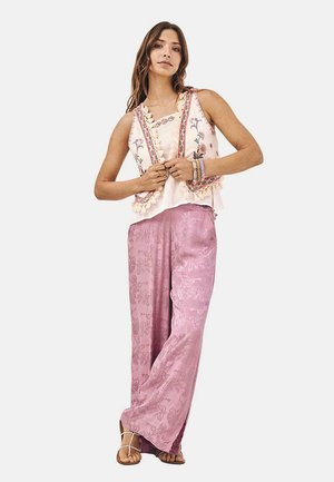 Pantalones de pierna ancha de patrón floral en rosa claro combinados con una blusa sin mangas color crema que presenta bordados coloridos y acentos de pompones.