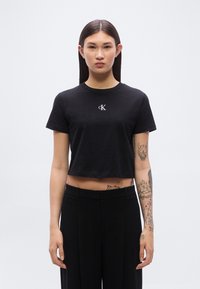 Μα ύρο κοντομάνικο μπλουζάκι από βαμβάκι με στρογγυλή λαιμόκοψη και κοντά μανίκια. Διαθέτει μικρό λευκό λογότυπο στο στήθος. Φοριέται με μαύρο ψηλόμεσο παντελόνι.