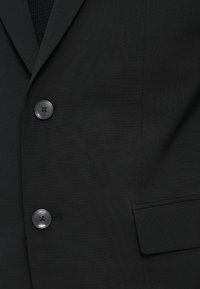 Blazer nero con tessuto liscio, due bottoni e una tasca sul petto con una sottile texture e rever strutturati.