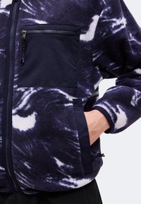 Ναυτικό μπλε και λευκό fleece μπουφάν με μαύρη τσέπη στο στήθος με φερμουάρ και χέρι τοποθετημένο στην πλαϊνή τσέπη.
