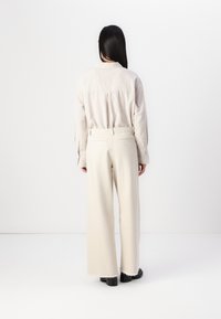 Lightweight beige long-sleeve shirt with a back yoke detail, paired with high-waisted cream wide-leg pants featuring raw hem and back pockets.