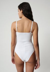 Costume da bagno intero bianco con spalline sottili, design senza cuciture e aperture per le gambe alte, che mette in mostra una texture di tessuto liscia.