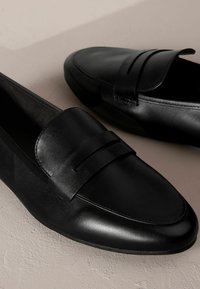 Mocassini in pelle nera con texture liscia, punta arrotondata e dettagli cuciti. Presentano una fascia larga sulla parte superiore per un tocco di design in più.