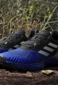 Juoksukengät, joissa on musta verkkomateriaali päällä, sininen synteettinen pohja ja harmaat yksityiskohdat. Ominaisuuksia ovat teksturoitu pinta ja tiukka nauhoitusjärjestelmä.