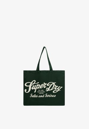 Donkergroene draagtas met beige sierlijke tekst “Super Dry Co. Inc. Yokohama Japan Sales and Service” en twee schouderbanden.