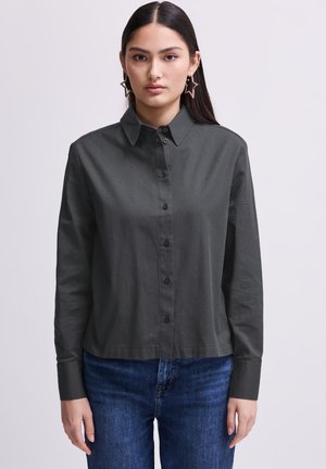 Donkergroene overhemden gemaakt van katoen, met een klassieke kraag en kleine geborduurde stippen. Gecombineerd met blauwe denim jeans.