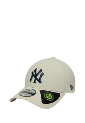 Beige baseball cap with a navy embroidered NY logo, curved brim, and adjustable strap. Includes branding labels on the side and visor.