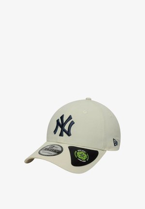 Beige baseball cap with a navy embroidered NY logo, curved brim, and adjustable strap. Includes branding labels on the side and visor.