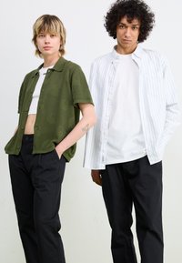 Olive green knitted short-sleeve shirt, black pants, striped white button-up shirt, and black pants. Casual fit, plain textures, and patterns.
