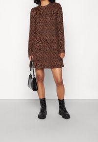 Robe longue à manches longues imprimée léopard marron avec une coupe décontractée, associée à des bottes de combat noires et un sac à main noir texturé.