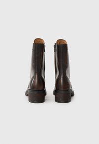Bottines en cuir marron avec une finition lisse, fermeture éclair et un talon empilé. Présente des coutures décoratives et un design à bout arrondi.