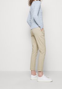 Svetle modrý svetr s pleteným vzorem, béžové slim-fit kalhoty a bílé tenisky. Oblečení obsahuje svetr s texturou a design kalhot s tapered nohavicemi.