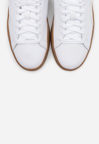 Pair of white sneakers with white laces and brown rubber soles, viewed from above on a white background.