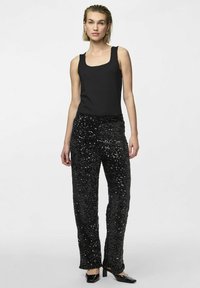 Haut sans manches noir, au design ajusté. Associé à un pantalon à sequins noirs étincelants, à jambe droite, avec une texture douce et des accents brillants. Des chaussures noires complètent la tenue.
