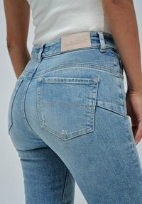 Vaqueros de mezclilla azul claro con un diseño ajustado, que incluyen bolsillos traseros, un ligero desgastado y una etiqueta de cuero beige en la cinturilla que dice "SALSA JEANS."