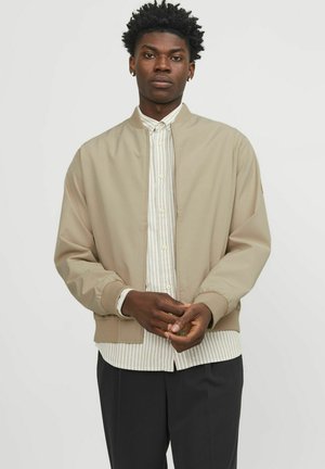 Khaki bomber jacket with ribbed cuffs and hem, unzipped over a light striped shirt. The fabric is smooth with a matte finish.