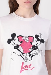 White cotton T-shirt featuring a graphic of Mickey and Minnie Mouse holding hands inside a glittery pink heart, with "Love" text below.