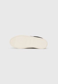 Semelle de sneaker noire avec une semelle extérieure en caoutchouc blanc texturé. Présente des rainures pour l'adhérence et le logo "Calvin Klein" sur le côté.