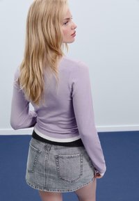 Pull ajusté violet clair à manches longues, assorti à une jupe en denim grise taille haute avec une ceinture rayée blanche et noire.