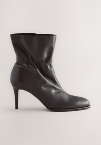 Stivaletto nero in pelle con punta appuntita e tacco alto e sottile, con dettaglio elastico arricciato intorno alla caviglia.