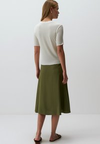 Biała, prążkowana bluzka z krótkim rękawem w połączeniu z oliwkową, spódnicą do kolan. Miękka tekstura, falbaniasty dekolt i zwiewny krój.