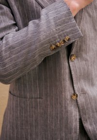 Blazer grigio a righe con una texture sottile, polsino a quattro bottoni e bottoni abbinati, con una tasca singola sul davanti.