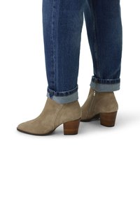 Beige Wildleder-Ankle Boots mit spitzer Zehe und gestapeltem Holzabsatz, ausgestattet mit einem seitlichen Reißverschluss und kombiniert mit hochgekrempelten blauen Denim-Jeans.