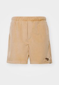 Shorts en velours côtelé beige avec une taille élastique, dotés de poches latérales et d'un logo brodé marron foncé sur le bas à gauche.
