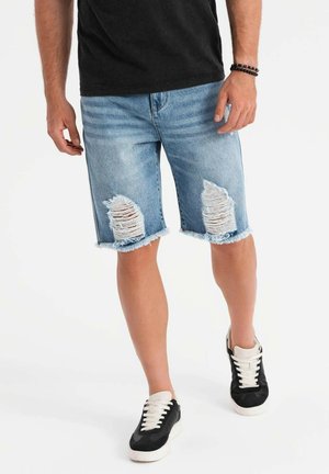 Shorts en denim bleu clair avec des ourlets effilochés, présentant de grandes zones usées. Associés à des baskets noires et blanches.
