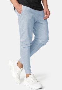 Helle blaue Jogginghosen aus weichem Stoff, mit schmal zulaufenden Beinen und Seitentaschen, kombiniert mit weißen Sportschuhen.