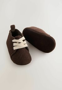Brune strikkede babysko med en tekstiloverdel, designet med en hvid snørebåndslukning og en blød brun ruskindsål. Struktureret ribbet mønster.