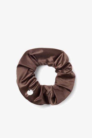 Chouchou en satin marron avec des plis doux et une petite étiquette ronde en métal attachée sur un fond blanc.