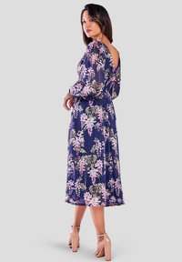 Marineblauwe jurk met bloemenpatroon, lange pofmouwen, open rug en midi-lengte. Voorzien van subtiele plooien en een elastische tailleband.