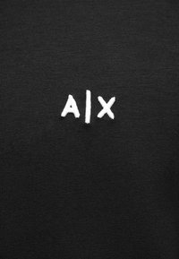 Čierna bavlnená tkanina s hladkou textúrou, na ľavej strane s bielymi vyšívanými písmenami "AIX". Jednoduchý, čistý dizajn.