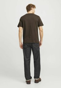 Camiseta de algodón marrón oscuro con cuello redondo, combinada con jeans de lavado oscuro que presentan puños enrollados y costuras en contraste en los bolsillos traseros.