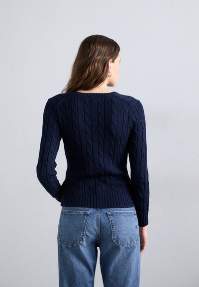 Navy cable-knit sweater features ribbed hem and cuffs. Pairing with faded blue jeans, the back shows a rounded neckline and textured pattern.