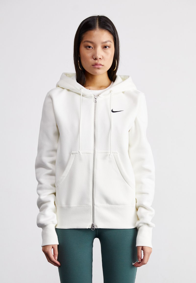 Sweatshirt branco com fecho zip, feito de um tecido macio, apresentando um capuz grande, bolsos frontais e um pequeno logo preto da Nike no lado esquerdo do peito.