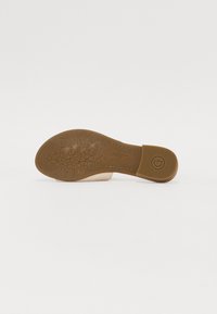 Scarpa slip-on beige con suola marrone texture, caratterizzata da motivi floreali e branding. Materiale superiore liscio, design con retro aperto.