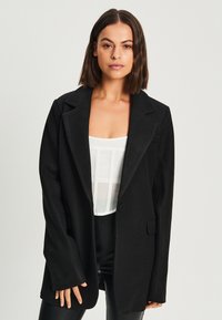 Blazer noir ajusté avec un col à revers, fermeture à un bouton et deux poches avant. Tissu texturé, coupe décontractée et manches longues.