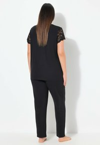 Zwart pyjama set met korte kanten mouwen. Zacht, gestructureerd materiaal en een ontspannen pasvorm. De broek heeft een rechte snit en een elastische tailleband.