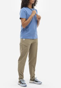 Jasnoniebieska bawełniana koszulka z grafiką po lewej stronie, w połączeniu z beżowymi spodniami cargo z wieloma kieszeniami i detalem logo.