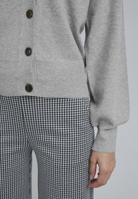 Grå stickad cardigan med knäppning, med ribbade manschetter; parat med byxor i svart och vitt hundstooth-mönster.