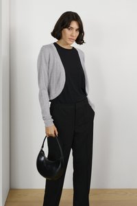 Gray cardigan with a soft texture, paired with a black top and black trousers. Holding a round black handbag. Minimalist design.