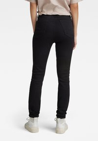 Jeans slim fit negros con una textura suave, que cuentan con dos bolsillos traseros y detalles de costura sutiles, combinados con zapatillas altas blancas.