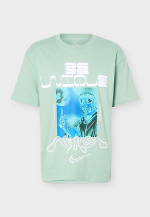 Svetlozelené tričko Nike so štýlovým nápisom "Be Unique" a modro tónovanou grafikou osoby v okuliaroch ukazujúcej nahor.