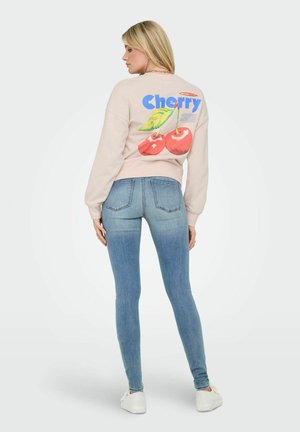Sweatshirt rose clair avec un motif de cerise au dos. Assorti à un jean skinny bleu et des baskets blanches. Tissu doux et coupe décontractée.