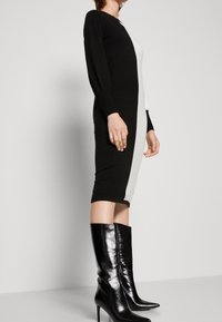 Stickad klänning med långa ärmar, med svart och vit färgblockering. Buren med knähöga svarta stövlar, slät textur, figurnära form.