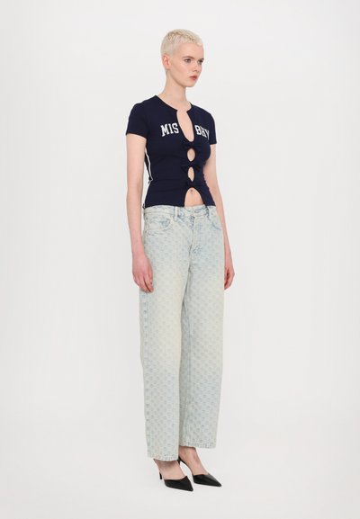 Navy short-sleeve top with lettered design and button details, paired with light wash, patterned wide-leg jeans and black pointed heels.
